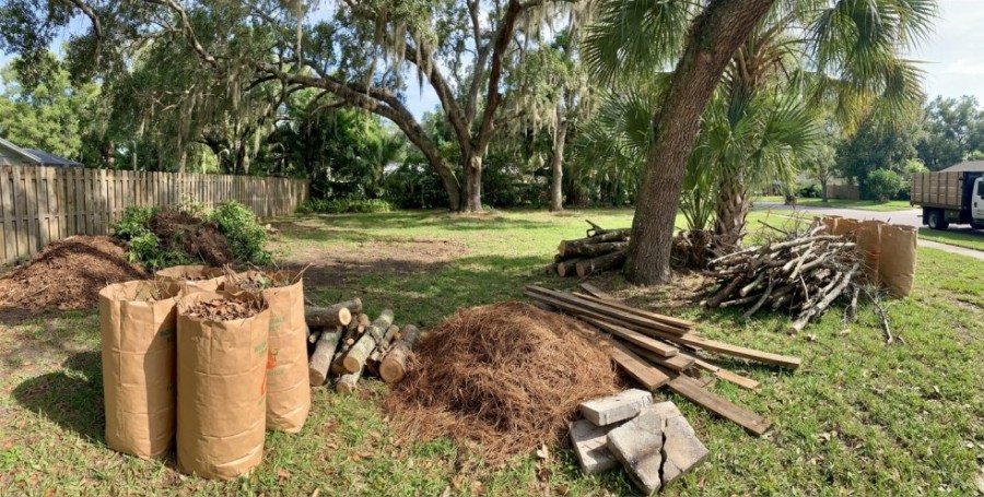Yard waste piled in a Tampa yard, including leaf bags, branches, logs, boards, and broken bricks