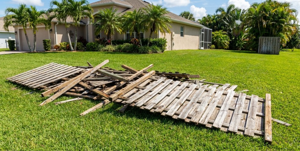 Broken wooden fence boards lying on a Florida lawn beside a home